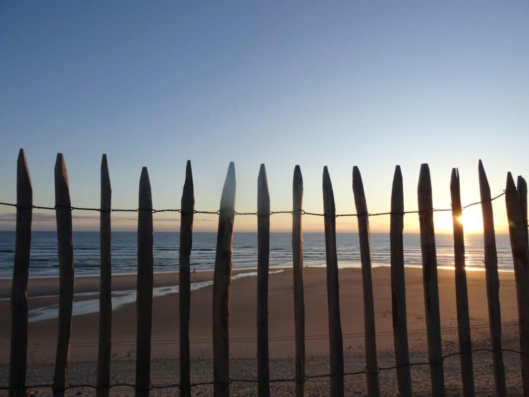 The sun is setting behind a fence on the beach