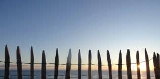 The sun is setting behind a fence on the beach
