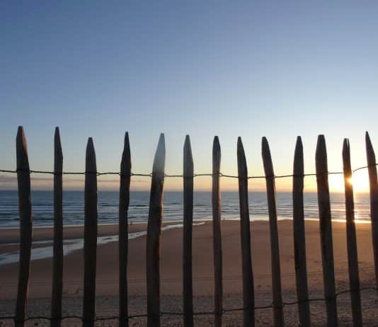 The sun is setting behind a fence on the beach